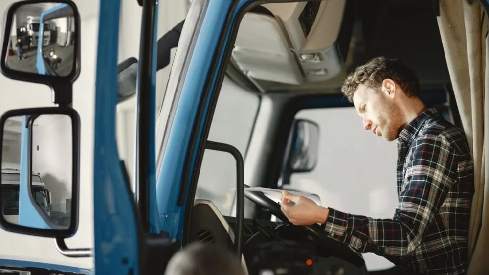 commercial-truck-driver-reviewing-paperwork Commercial truck driver reviewing paperwork while sitting inside a blue truck cab
