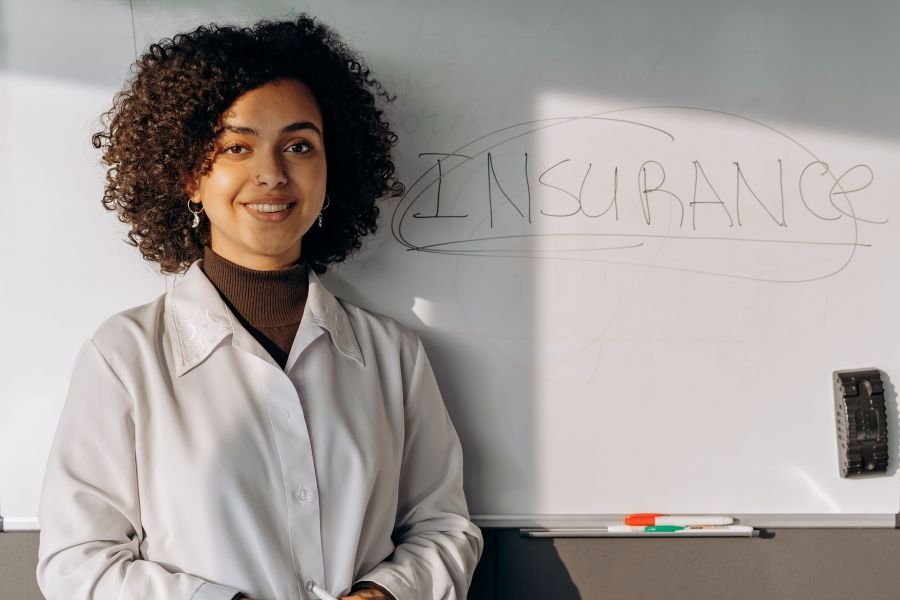 employer-sponsored-health-insurance Woman standing beside a whiteboard with the word insurance written on it