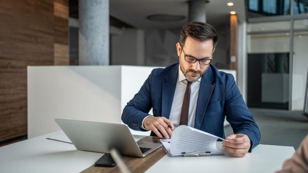 professional-liability-client-contract-review Business professional reviewing printed documents at a desk with a laptop.