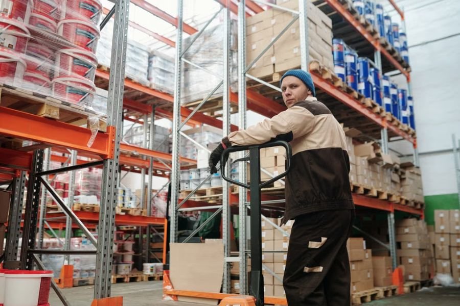 warehouse-worker-workers-compensation Warehouse worker standing with a pallet jack between storage racks